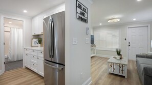 A modern kitchen with white cabinetry, a stainless steel refrigerator, and a sign that reads "RELAX AND UNWIND".
