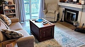 A living room with a sofa, armchair, coffee table, and a fireplace. There is a balcony with curtains and a view outside. - 4105  Slopes & Spokes Perfect Location (Beech Mountain)
