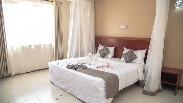 Una habitación de hotel con una cama grande, cortinas blancas y un cabecero de madera.