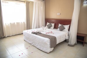 Een hotelkamer met een groot bed, witte gordijnen en een houten hoofdbord.
