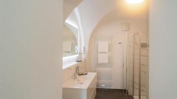 Ein schmaler Flur führt zu einem Badezimmer mit Waschbecken, Spiegel und Dusche.