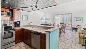 A modern kitchen with a central island, built-in appliances, and a dining area with a view. - S Hampton 409 1 Br Oceanfront in Kingston, Pool (Myrtle Beach)