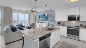 A modern kitchen with white cabinetry, stainless steel appliances, and a large island with a dishwasher. - Lighthouse 1104 by Liquid Life (Gulf Shores)