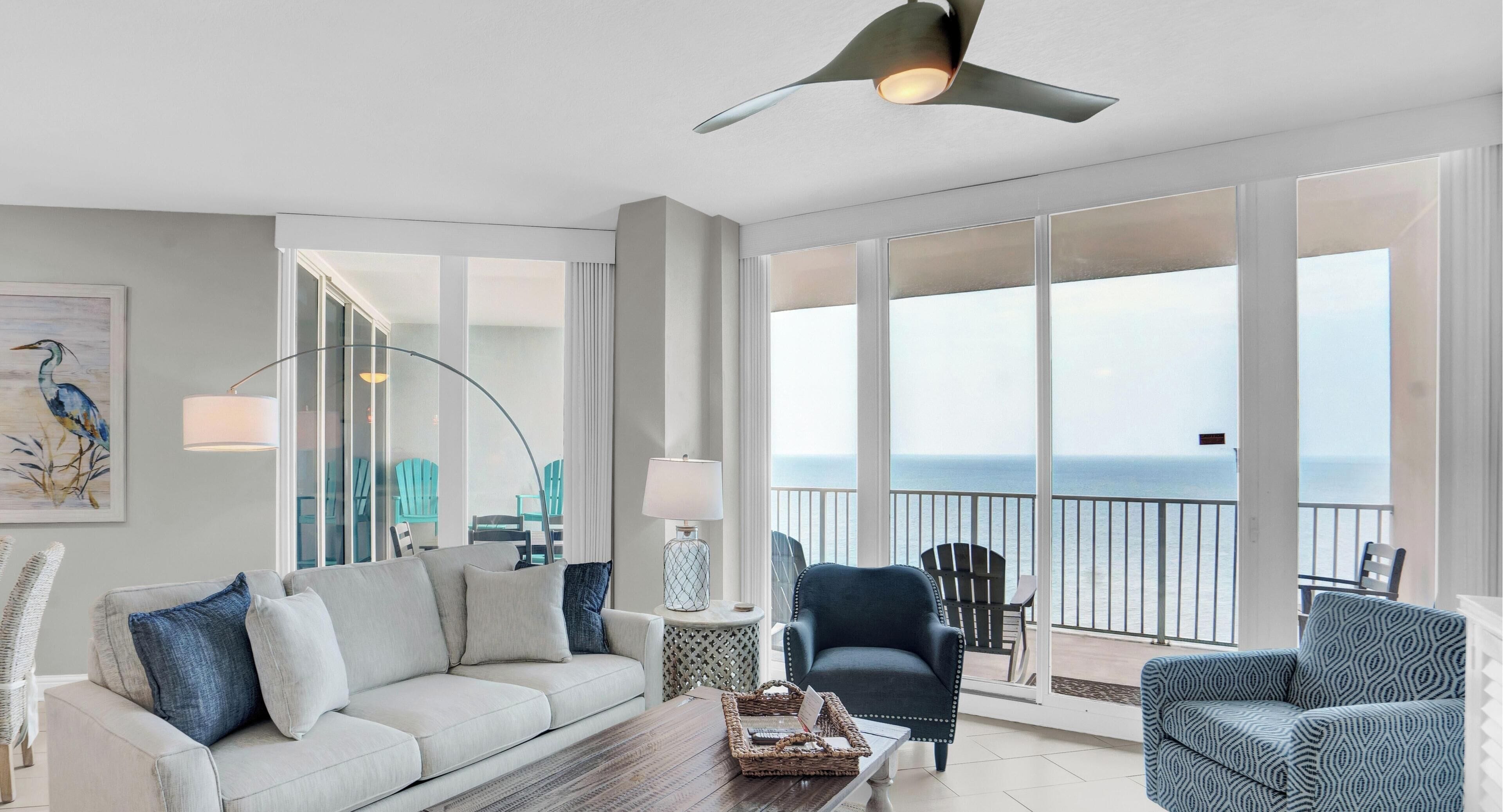 A spacious living room with a large window offering a view of the sea, a ceiling fan, and a modern light fixture.