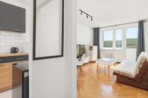 A modern living room with a sofa, a dining table, and a kitchen area with cabinets and appliances.
