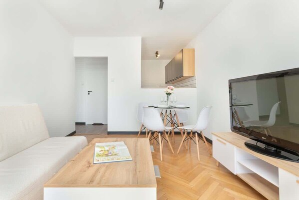 A modern living room with a sofa, coffee table, TV, and dining area with chairs and a small table.