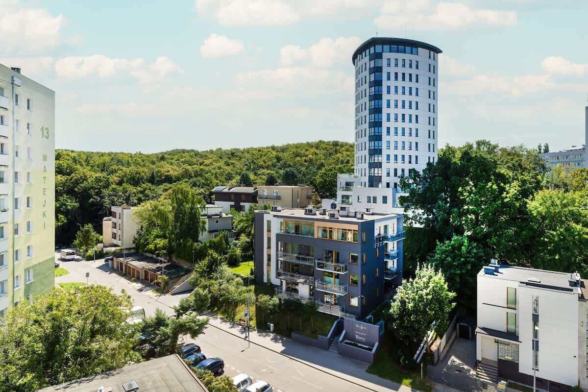 A modern building with a cylindrical tower, surrounded by other residential structures and greenery.