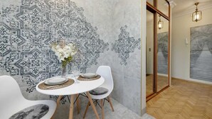 Un coin repas avec un mur orné d’un motif, une table ronde, des chaises blanches et un vase de fleurs.