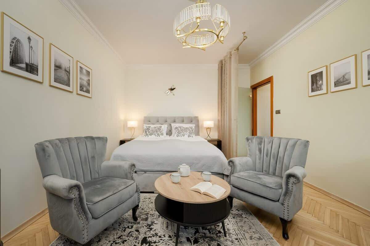 A hotel room with a bed, two armchairs, a round coffee table, and a chandelier.