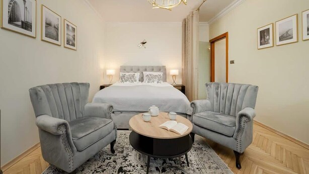 Une chambre d’hôtel avec un lit, deux fauteuils, une table basse ronde et un lustre.
