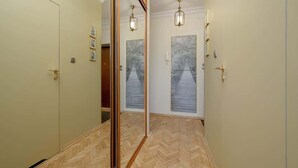 Un couloir avec un mur recouvert de miroirs, un plancher en bois et une porte dotée d’un panneau en verre.