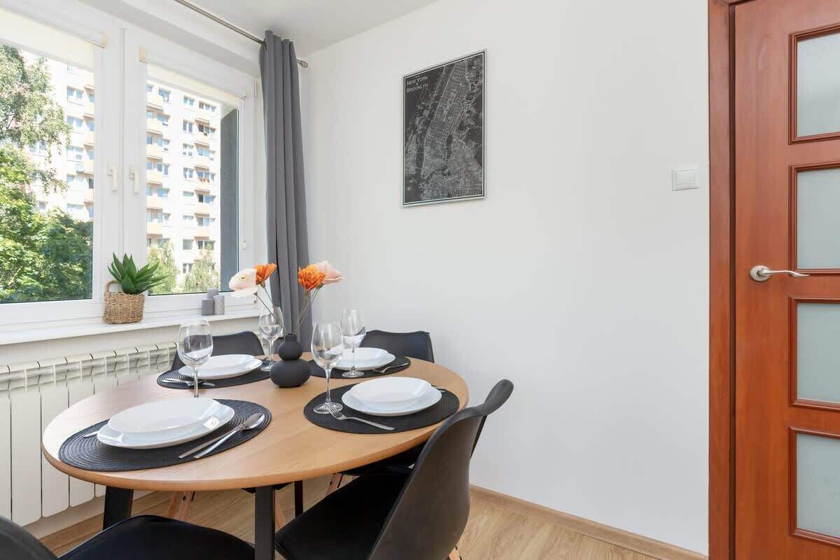 Un coin repas avec une table ronde dressée pour quatre personnes, une fenêtre donnant sur un immeuble et une porte dotée de panneaux en verre dépoli.