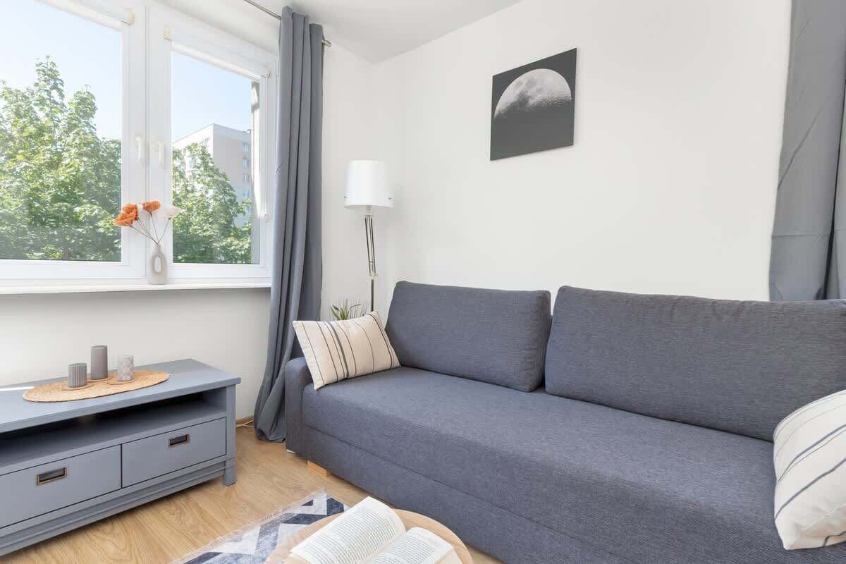 A modern living room with a grey sofa, a small side table, and a window with curtains.