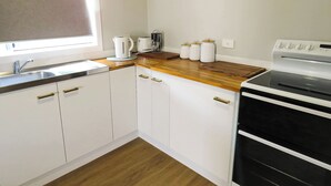 Una cocina con armarios blancos, encimera de madera, un fregadero, un hervidor, un tostador y un horno.