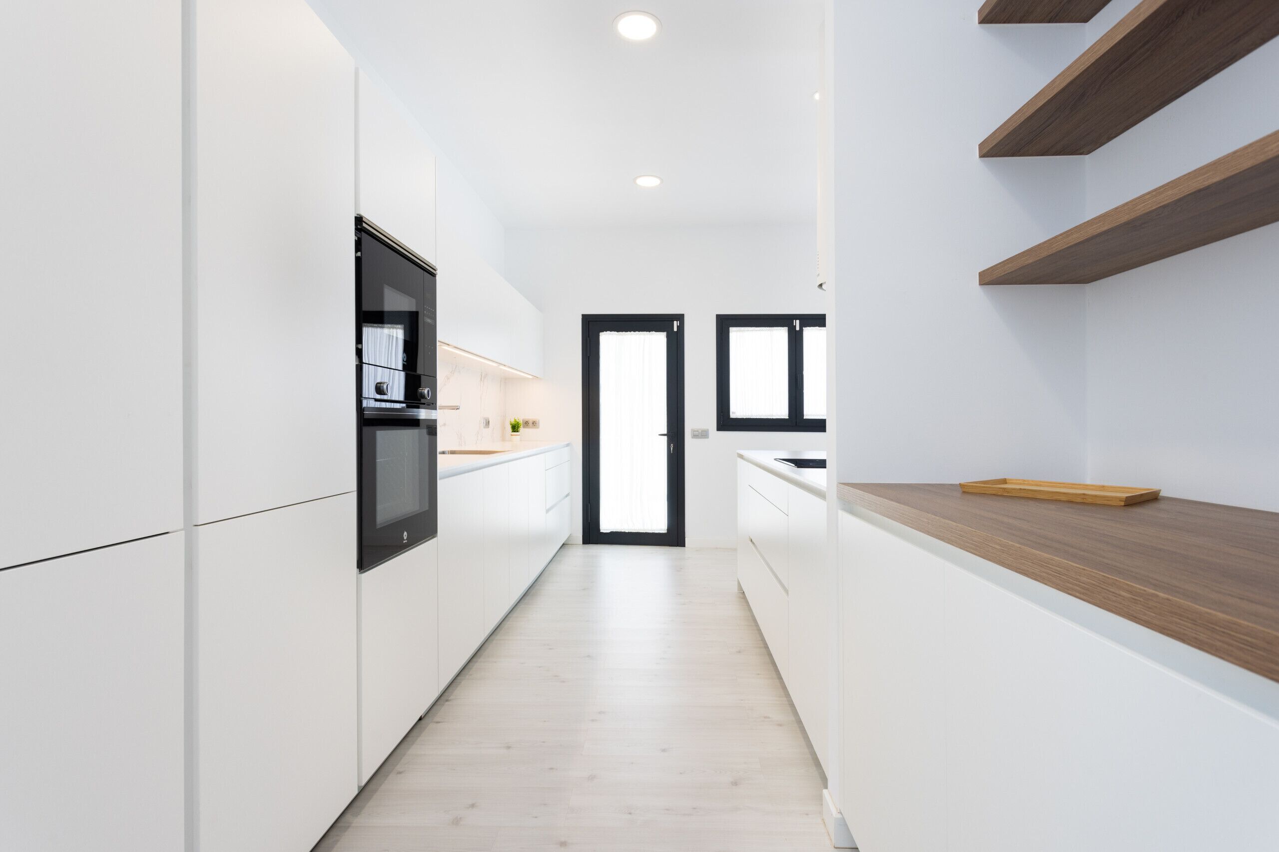A modern kitchen with white cabinetry, a wooden countertop, and a black-framed window.