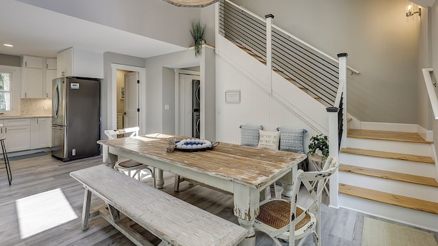 A modern kitchen with a stainless steel refrigerator, a wooden dining table with benches, and a staircase with wooden steps and a metal railing.