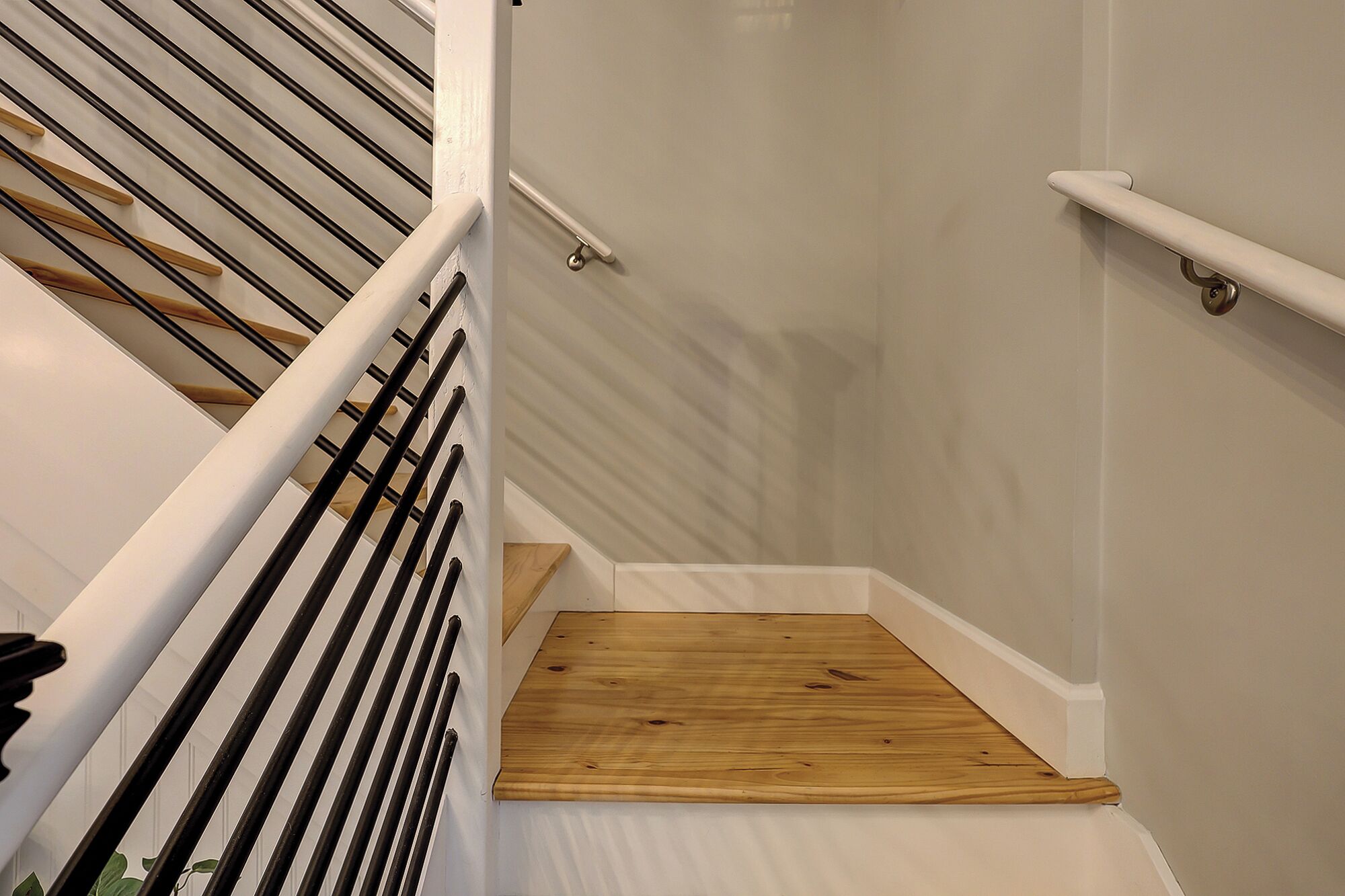 A staircase with wooden steps and black handrails, leading to a landing with a white wall and a wooden floor.