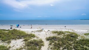 A beach with people walking and sitting, a clear sky, and the ocean in the background.