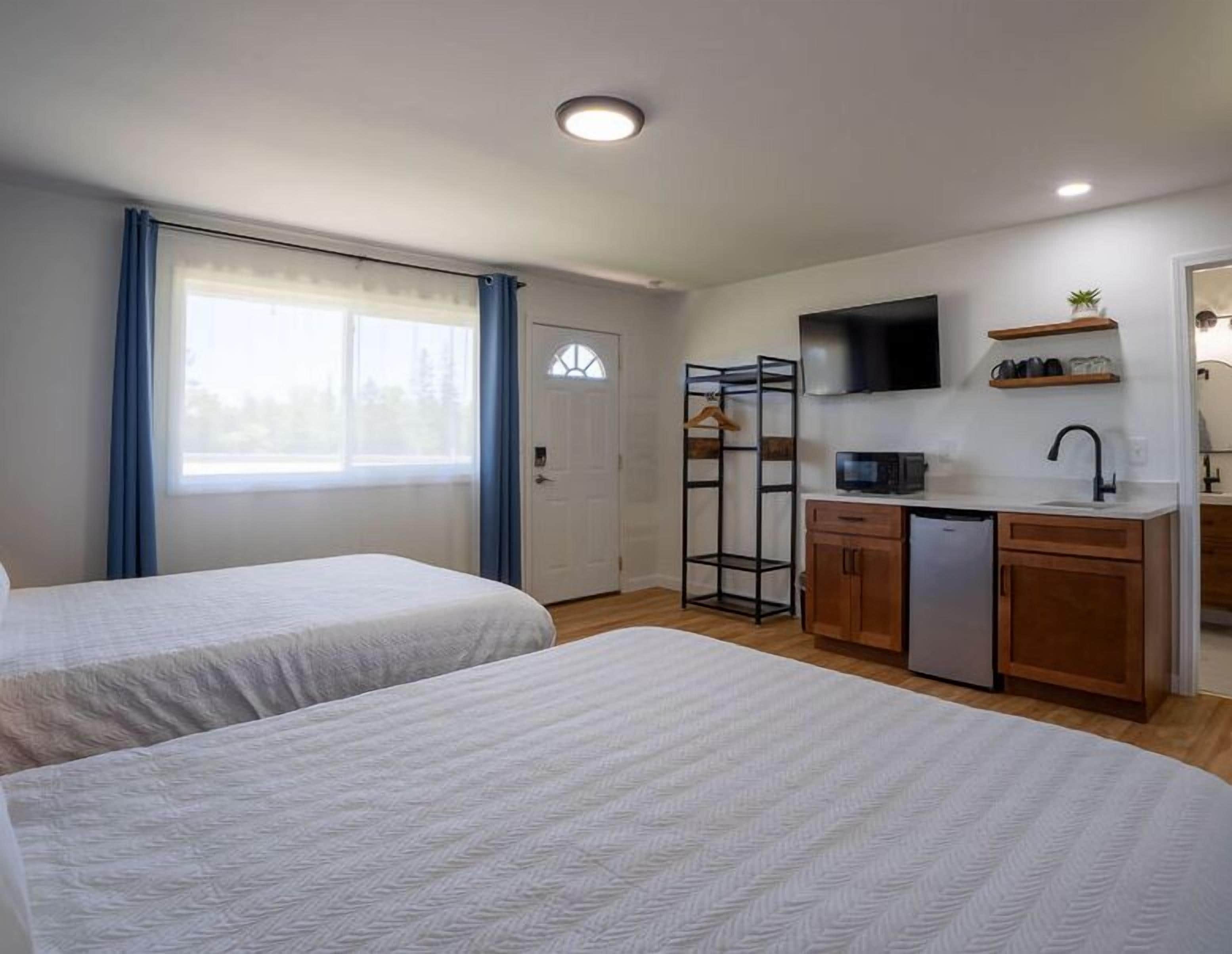 A room with two beds, a kitchenette, a TV, and a window with curtains.