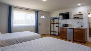 Ein Zimmer mit zwei Betten, einer Küchenzeile, einem Fernseher und einem fenster mit Vorhängen.