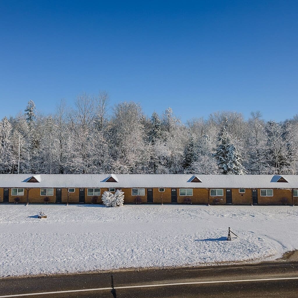 A motel with a row of rooms, a parking lot, and a snow-covered landscape.
