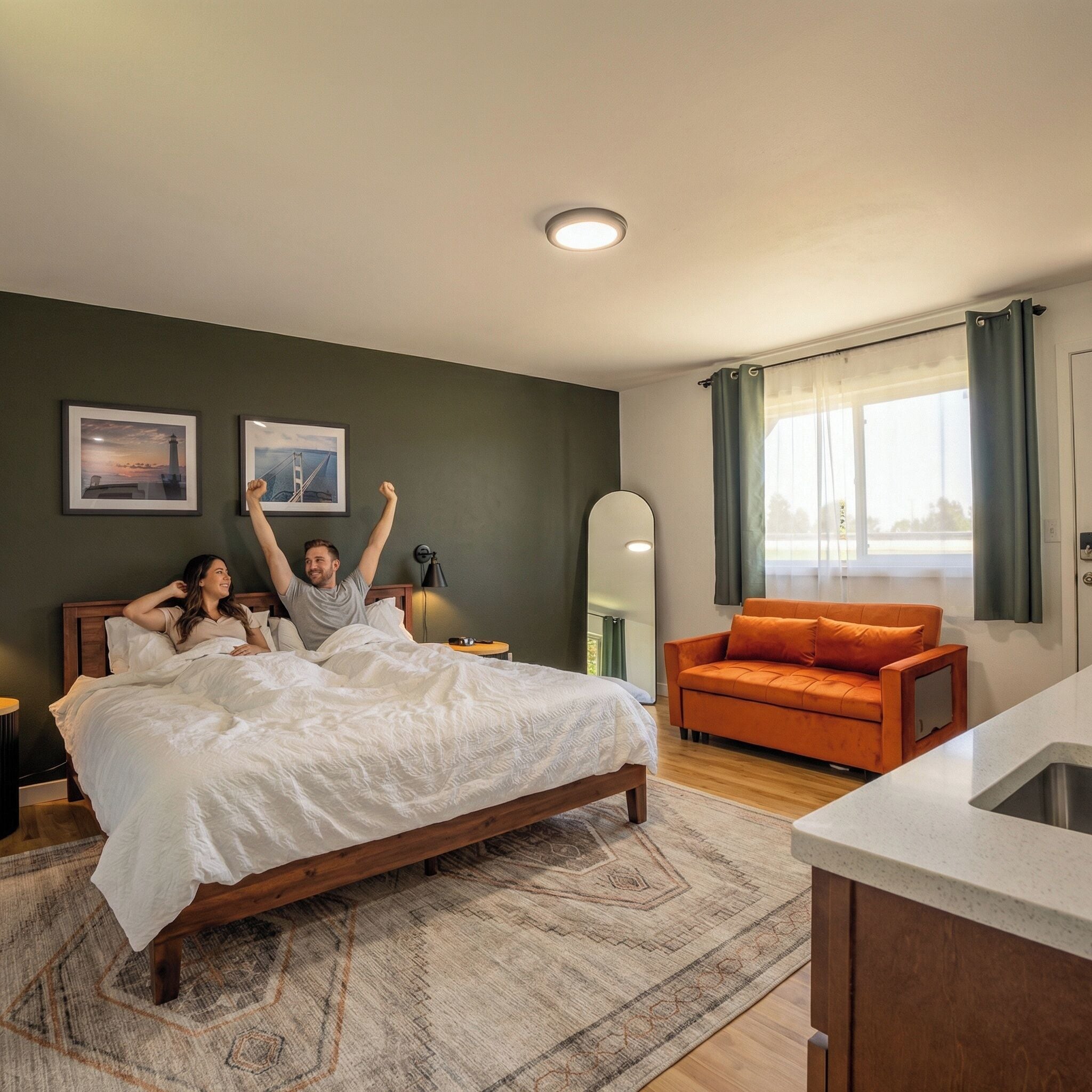 A bedroom with a bed, a nightstand, a mirror, a sofa, and a window with curtains.