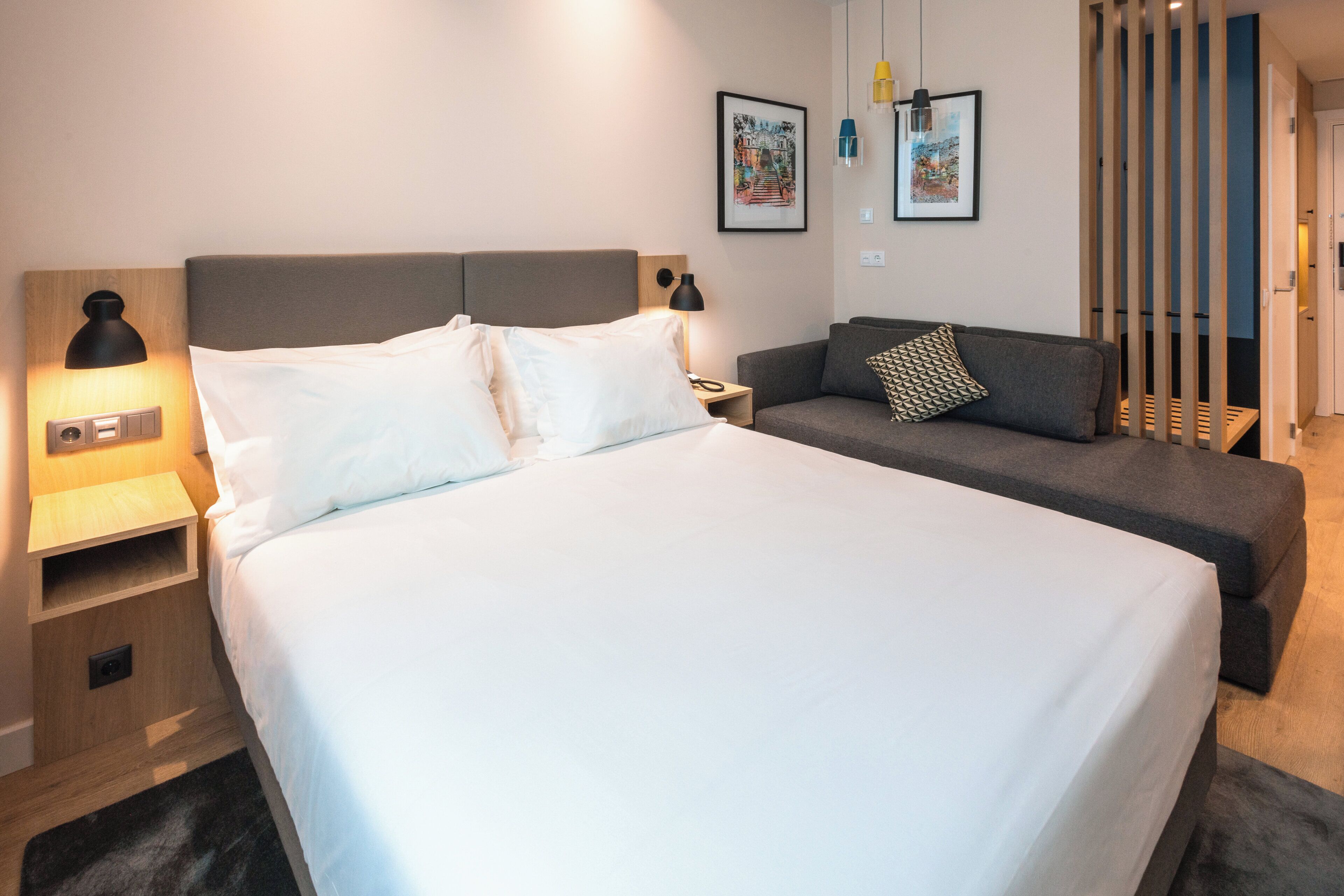 Une chambre d’hôtel avec un grand lit, une table de chevet, une commode, un canapé et une lampe fixée au mur.