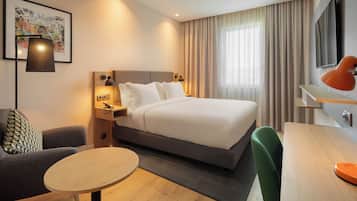 A modern hotel room with a large bed, a desk, a chair, a small table, and a TV.