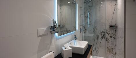 A modern bathroom with a glass-enclosed shower, a white sink, and a large mirror.