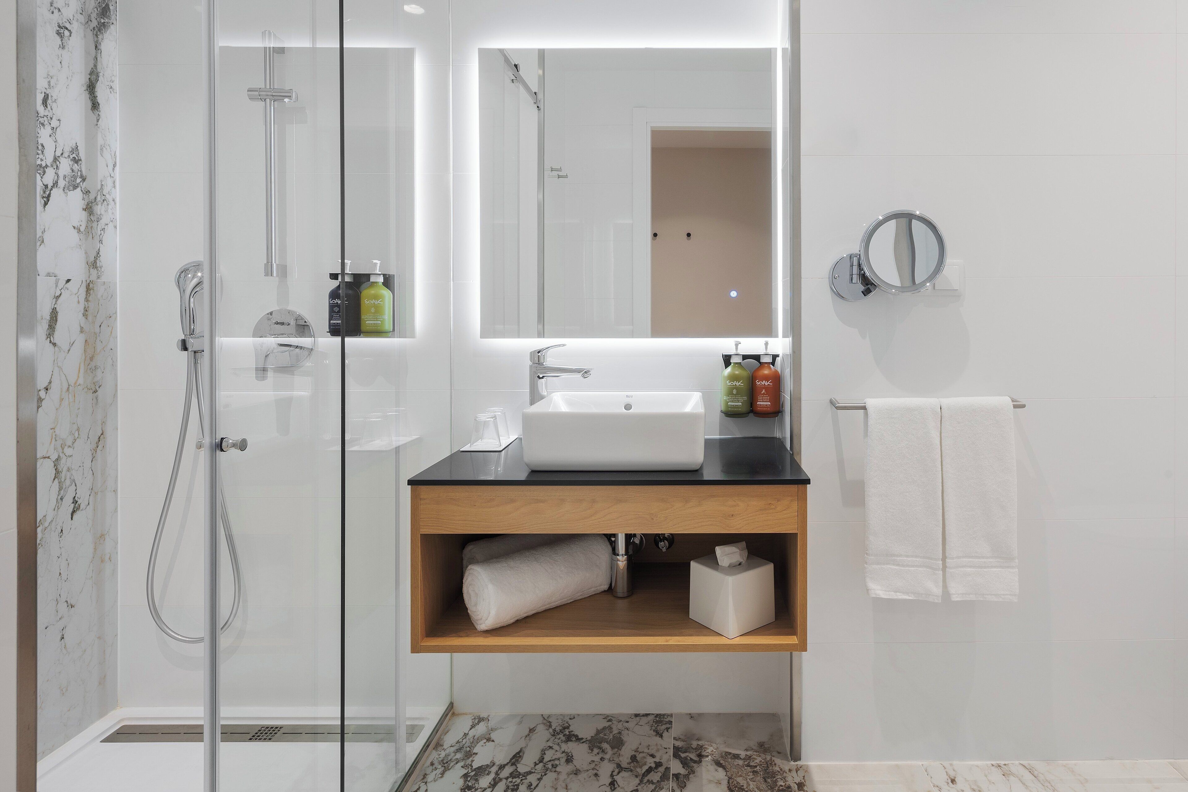Een moderne badkamer met een douche met glazen wanden, een witte wastafel en een houten meubel.