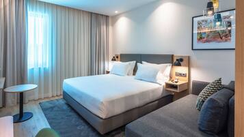 A hotel room with a large bed, a bedside table, a chair, a sofa, and a painting on the wall.