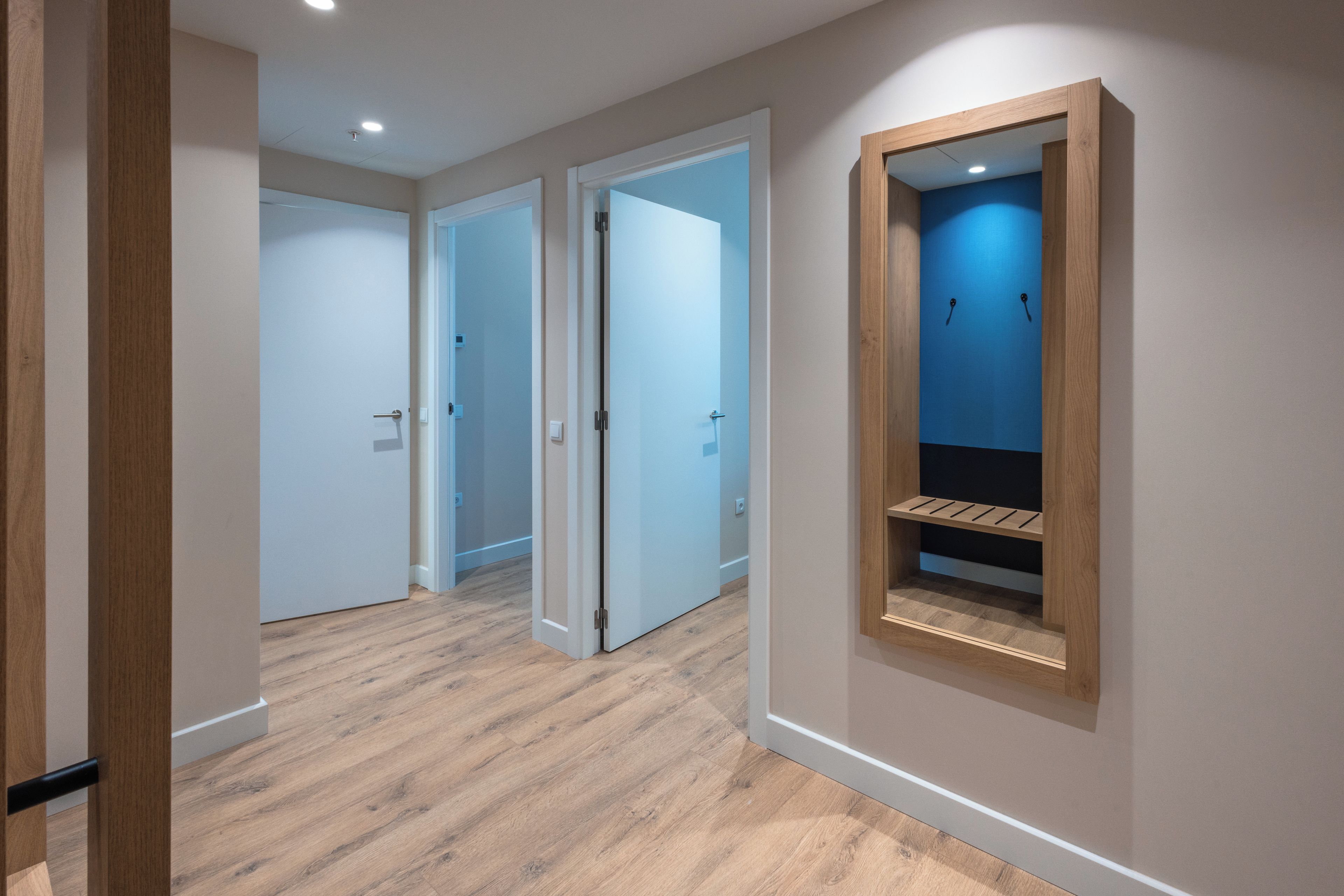 A hallway with wooden flooring, white walls, and a blue accent wall with a built-in shelf.