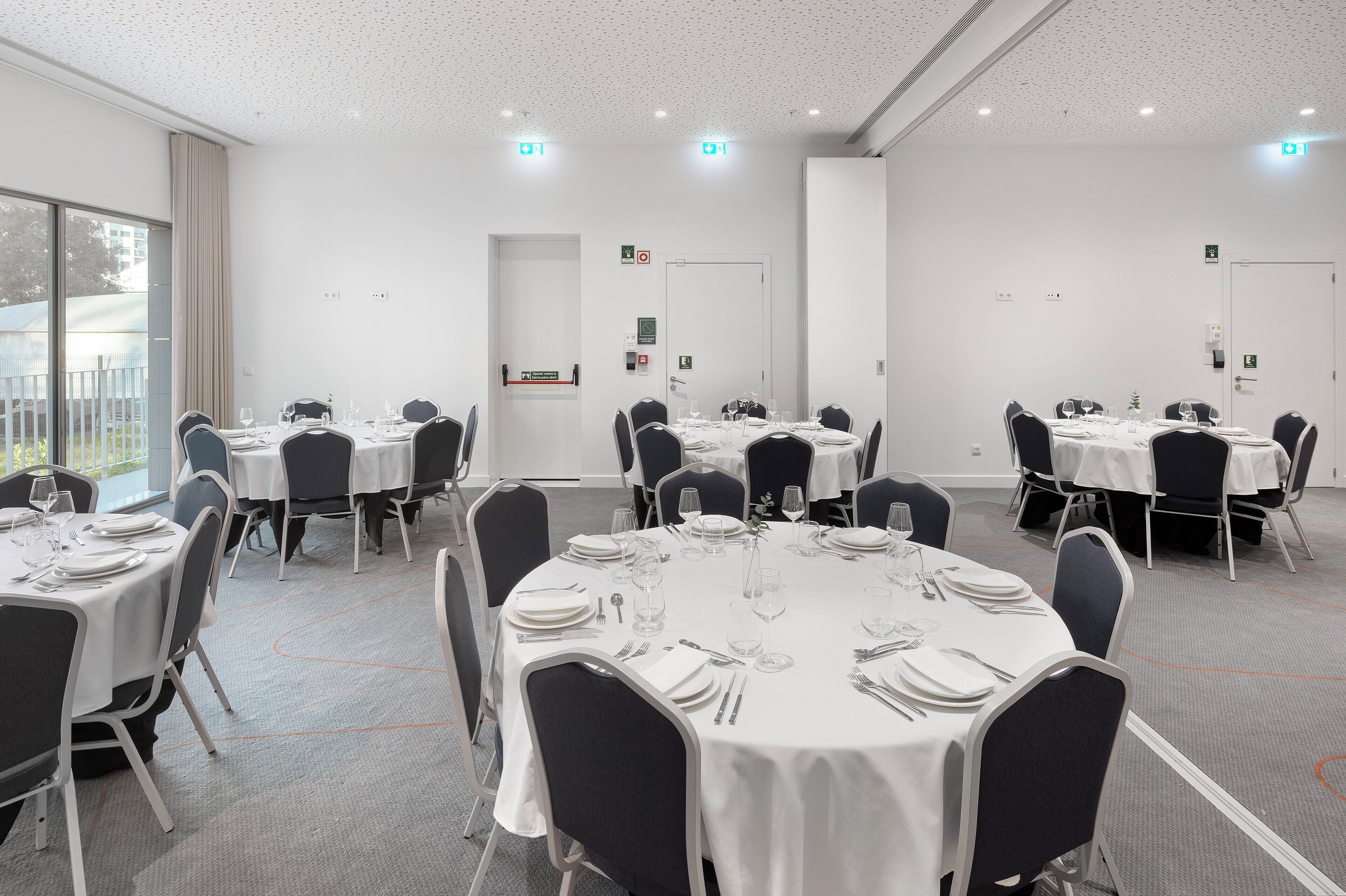 A conference room with round tables, black chairs, and white tablecloths.