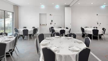 A conference room with round tables, black chairs, and white tablecloths.