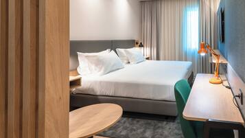 A modern hotel room with a large bed, a desk, a chair, and a small table.