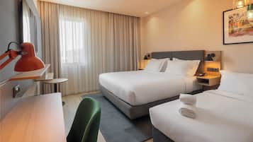 A hotel room with two beds, a desk, a chair, a TV, and a window with curtains.