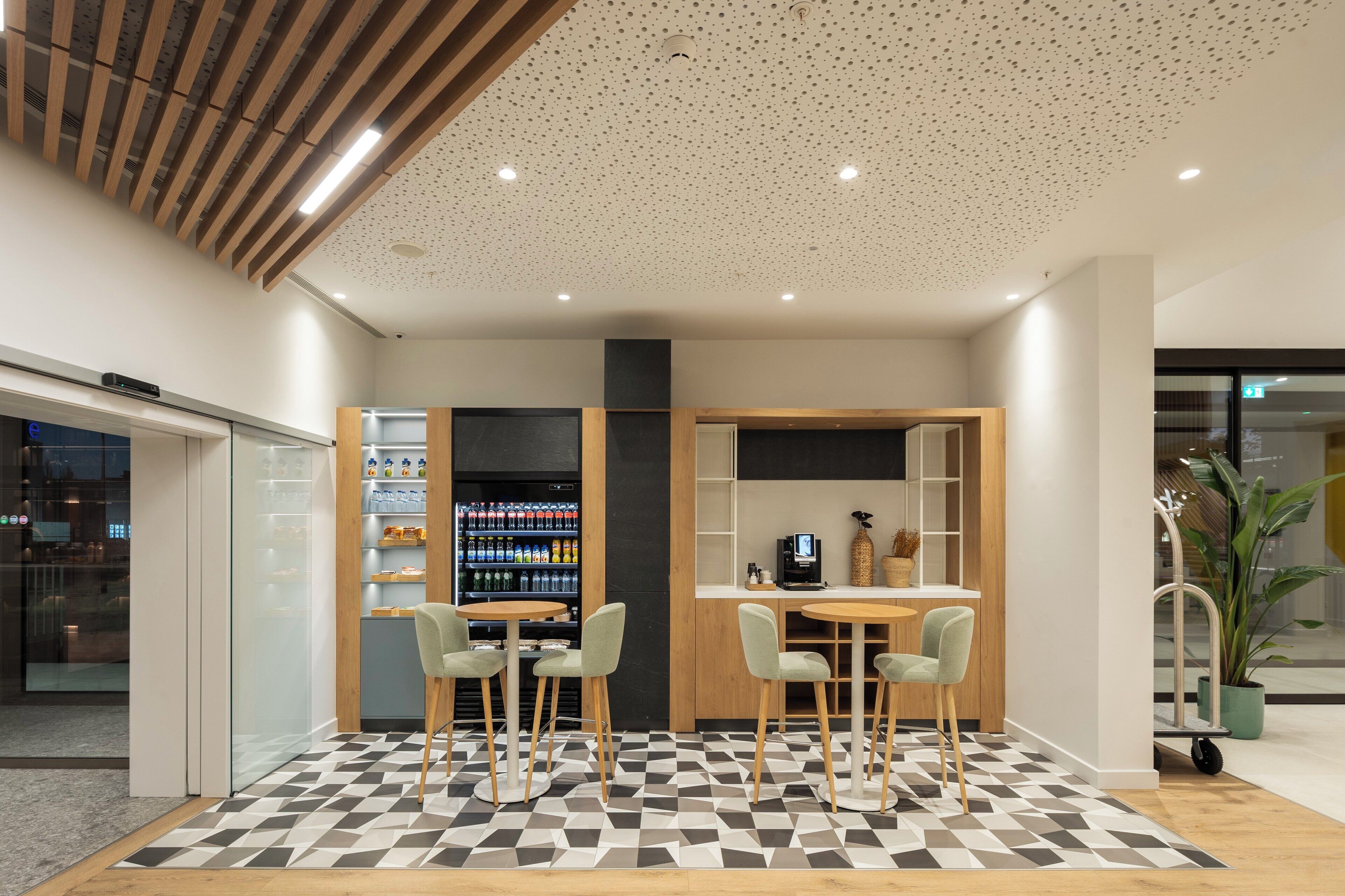 Um interior moderno com piso xadrez, banquetas, máquina de café e máquina de vendas.