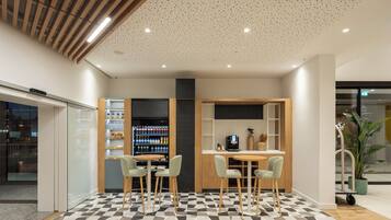 Um interior moderno com piso xadrez, banquetas, máquina de café e máquina de vendas.