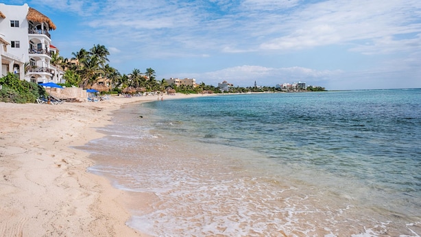Una playa con aguas cristalinas, palmeras y edificios con balcones.