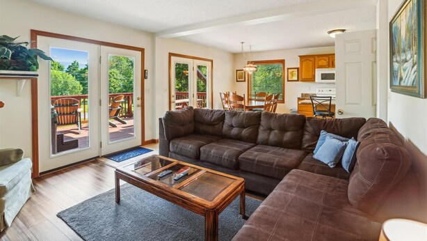 A living room with a brown leather sofa, a glass coffee table, and a dining area with wooden chairs and a table. There is a kitchen in the background with wooden cabinets and a microwave. - Enjoy some mountain time with your favorite canine at Alpine View! (Dry Fork)