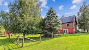 A red house with a sloped roof, surrounded by a fenced yard with green grass and trees. - Enjoy some mountain time with your favorite canine at Alpine View! (Dry Fork)