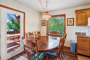 A dining area with a wooden table and chairs, a chandelier, and a view of the outdoors through a window with blinds. - Enjoy some mountain time with your favorite canine at Alpine View! (Dry Fork)