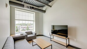 Ein modernes Wohnzimmer mit großem Fenster, grauen Sofas, einem Holztisch und einem Flachbildfernseher.