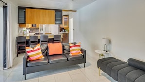 A modern living area with a sofa, a dining table, and a kitchen in the background. - Luxe Wimauma Home w/ Pool & Lake Views! (Wimauma)