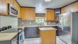 A kitchen with wooden cabinets, stainless steel appliances, a granite countertop, and a window with a view. - Luxe Wimauma Home w/ Pool & Lake Views! (Wimauma)