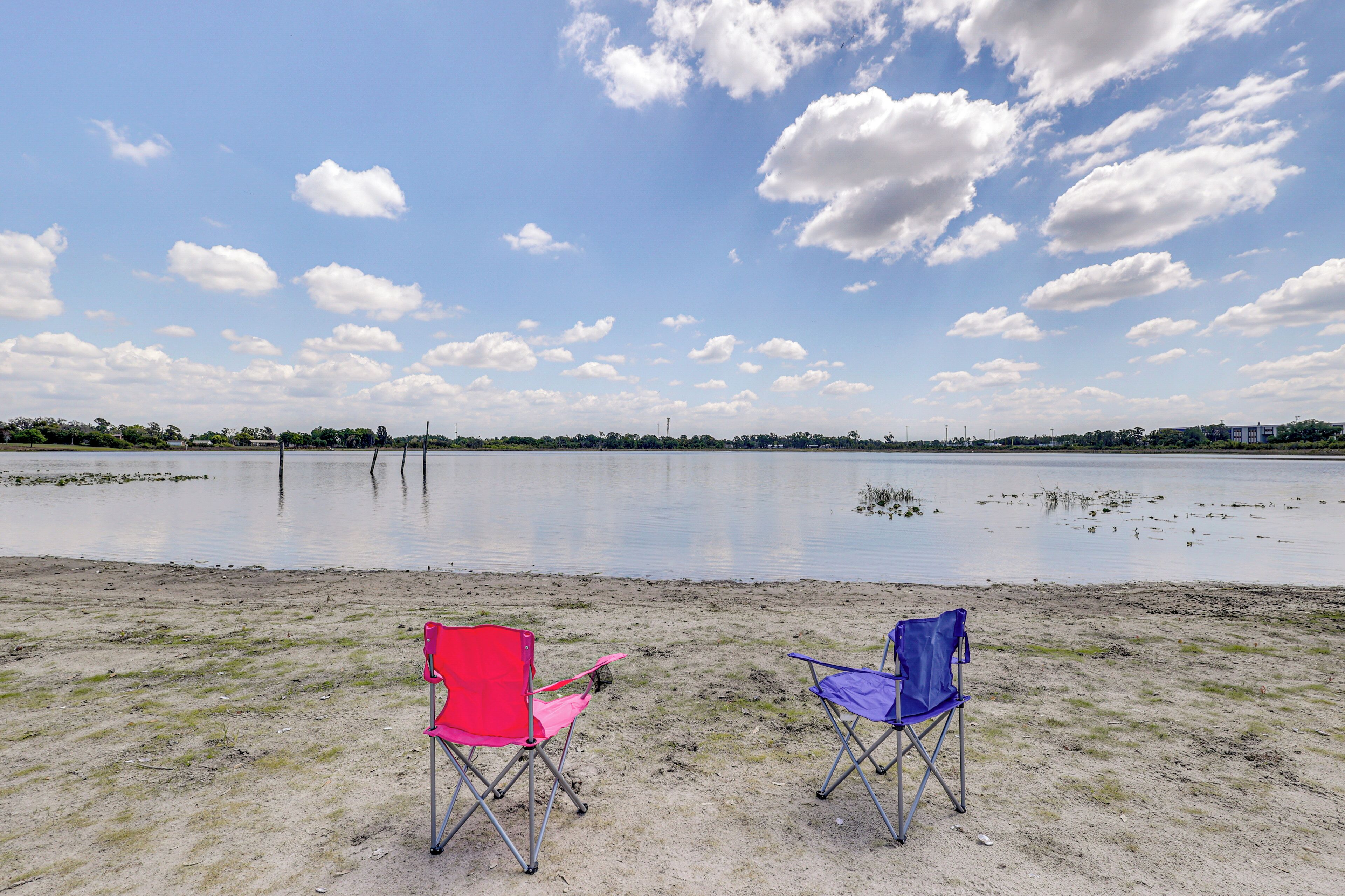Two folding chairs on a sandy shore with a lake and a clear sky.