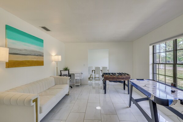 A modern living room with a sofa, a foosball table, and a painting on the wall. - Luxe Wimauma Home w/ Pool & Lake Views! (Wimauma)