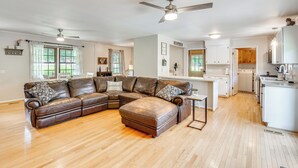 A spacious living room with a brown leather sectional sofa, a dining area, and a kitchen with white cabinets. - West Union Home w/ Saltwater Pool on 2 Acres! (West Union)