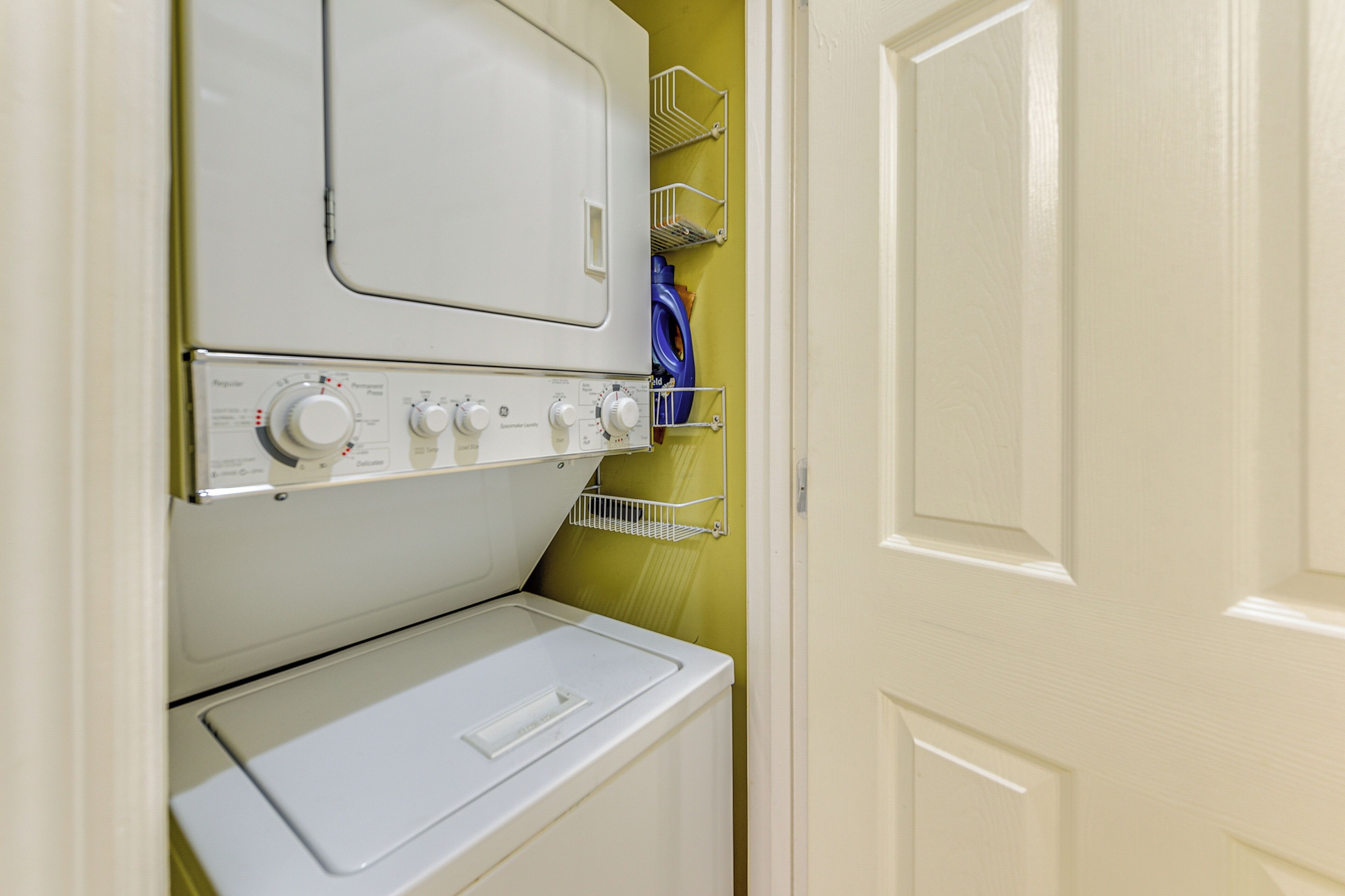 Un espace buanderie comprenant un lave-linge et un sèche-linge à chargement frontal, une étagère en métal avec un tuyau bleu et une porte blanche.