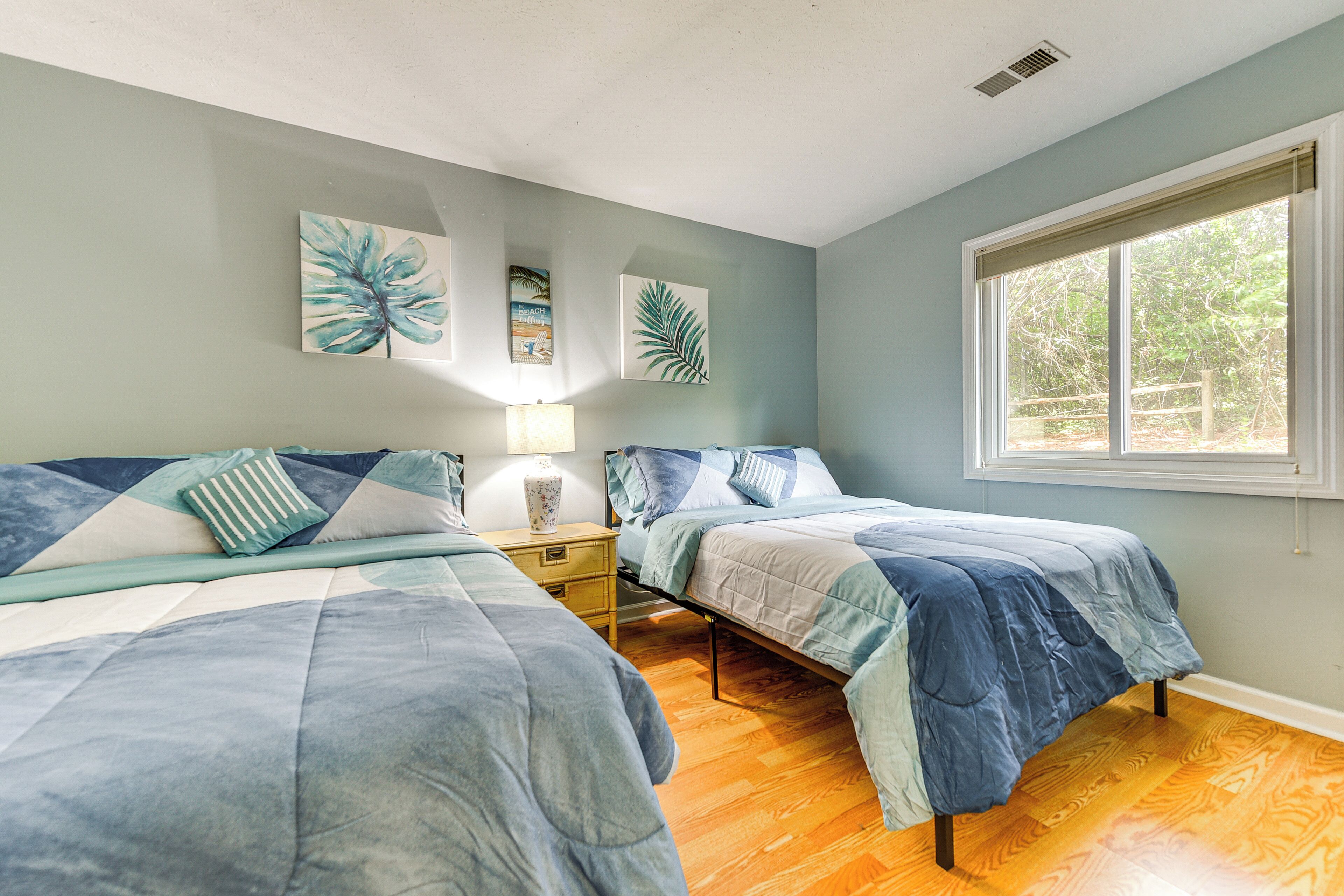 A bedroom with two beds, a window, and artwork on the wall.